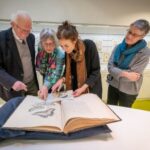 Jan Lindenbergh, diens dochter en bestuursvoorzitter Louise Fresco bekijken het boek van Merian.