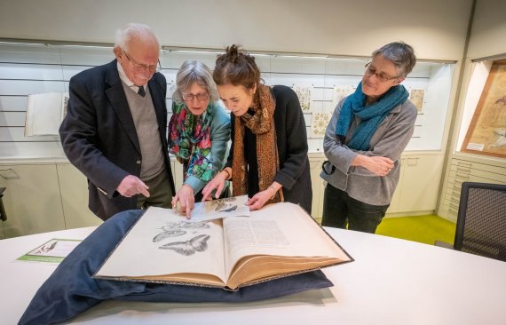 Jan Lindenbergh, diens dochter en bestuursvoorzitter Louise Fresco bekijken het boek van Merian.