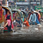 A flooded street, people are wading through the water