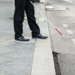 Picture of a person walking with a stick, on the side of the road