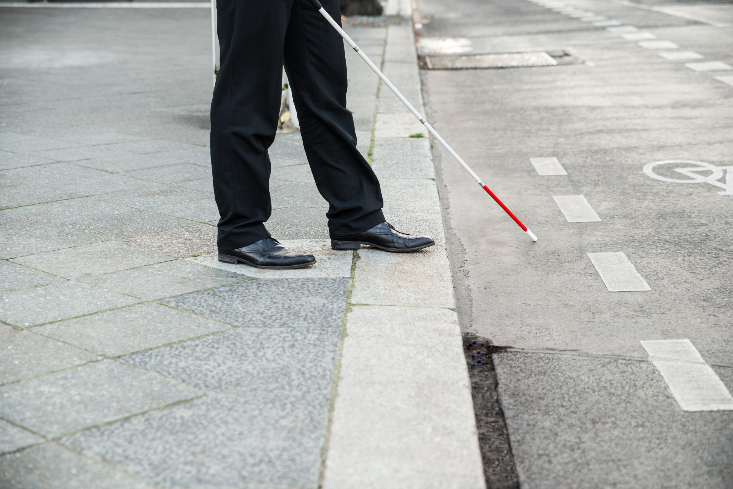 Picture of a person walking with a stick, on the side of the road