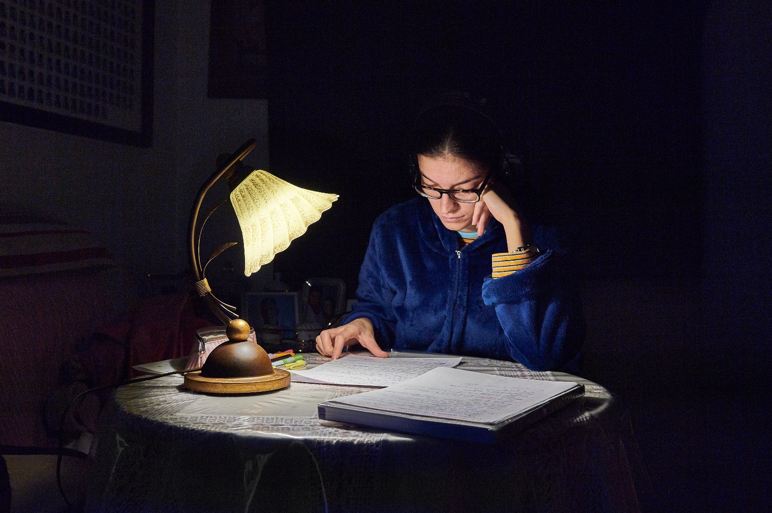 Vrouw leest boek aan tafel onder een lamp.