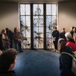 Deelnemers aan de wandeling bekijken het raam van de Wageningse Aula, met bovenin de koloniale aanduidingen 'Batavia' en 'Suriname'.