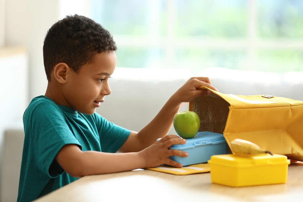 Jongetje haalt broodtrommel uit lunchtas.