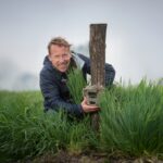 Patrick Jansen gehurkt in het gras bij een cameraval.